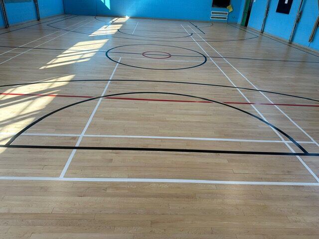 Hardwood floor fitting in a UK sports hall with crisp court lines, finished to withstand heavy footfall.
