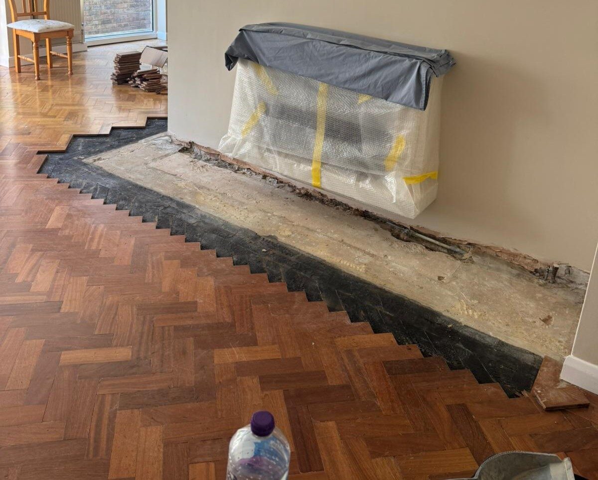Partially exposed solid wood herringbone parquet floor prepared for repairs and new Border Strips around a former fireplace area.
