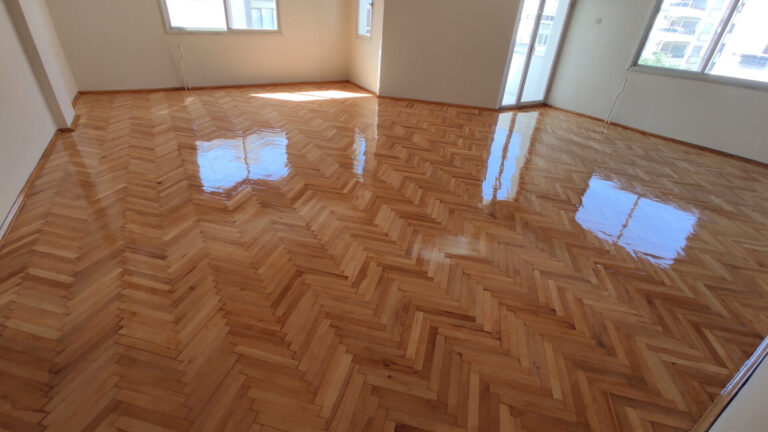 Freshly finished oak herringbone parquet wood floor after professional Herringbone Parquet Sanding, with a high-gloss surface reflecting natural light in an empty room.