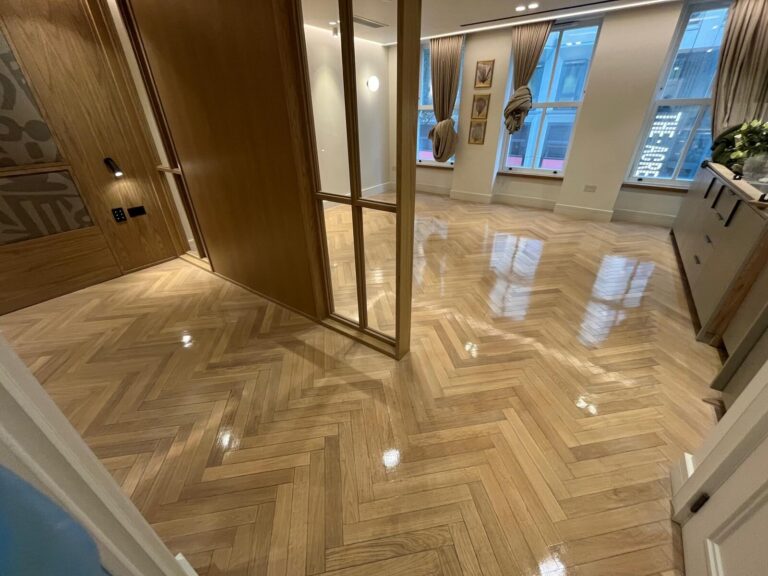 A modern interior featuring a reflective, high-gloss oak herringbone parquet floor completed after professional sanding.