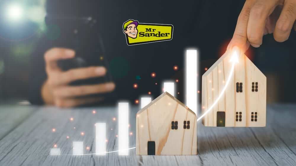 A hand pointing at a rising bar graph with model houses, symbolizing increased home value after hardwood floor restoration by Mr. Sander®.