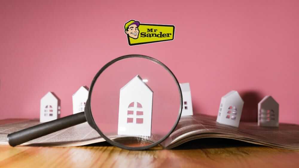 A magnifying glass focusing on a model house among other houses, symbolizing the importance of choosing the right hardwood floor restoration service.