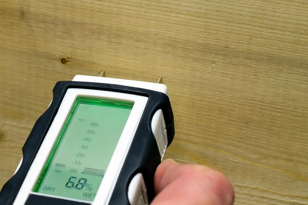 A close-up of a hand using a moisture meter on a hardwood floor to check the moisture level before sanding and refinishing. The meter shows a reading of 6.8%, ensuring the wood is dry enough for the refinishing process. The floor has been prepared for professional sanding and refinishing by Mr Sander®.
