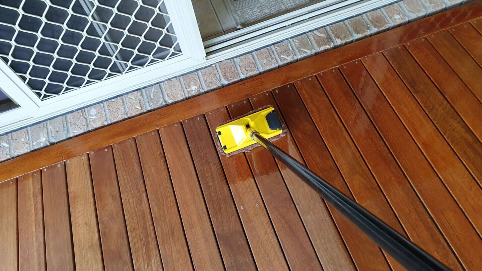 Joyful Decks finish being applied with a pad applicator to freshly sanded smooth hardwood timber decking beside a patio door, showing richer colour where the oil has soaked in.