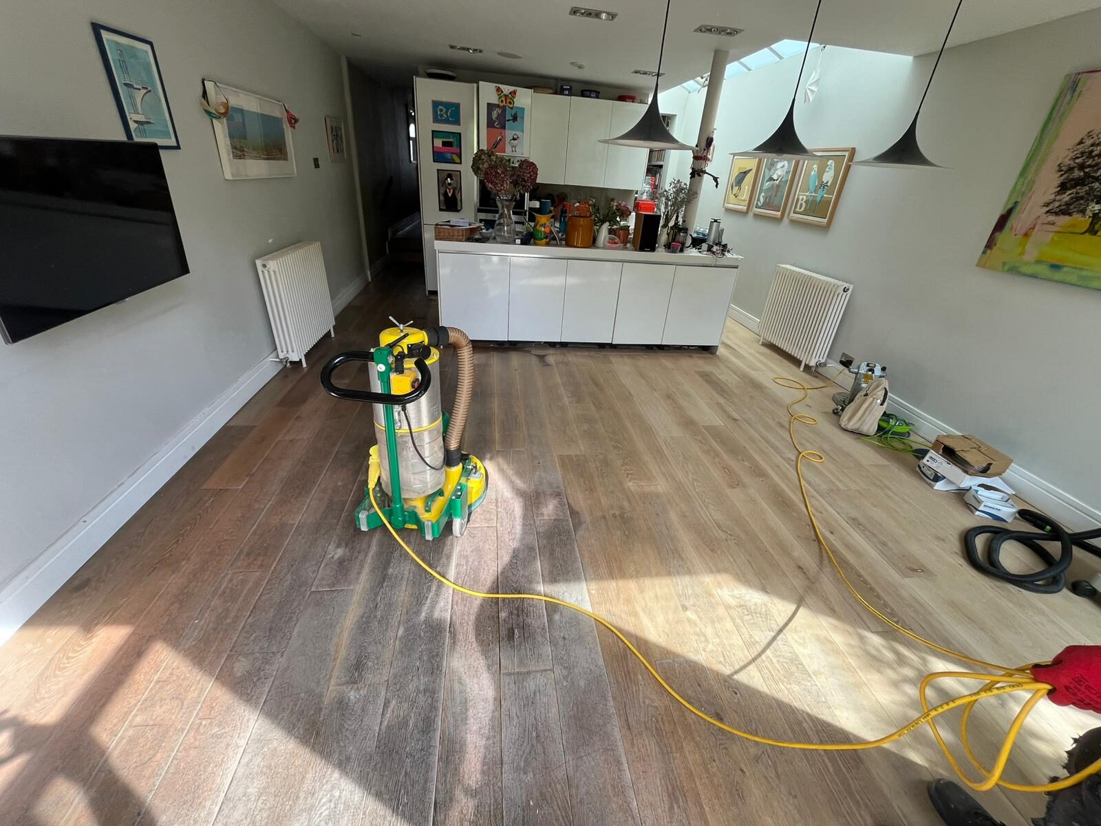 Oak kitchen floor in a Fulham home being sanded; a dust-free floor-sanding machine sits mid-room with power cable trailing.