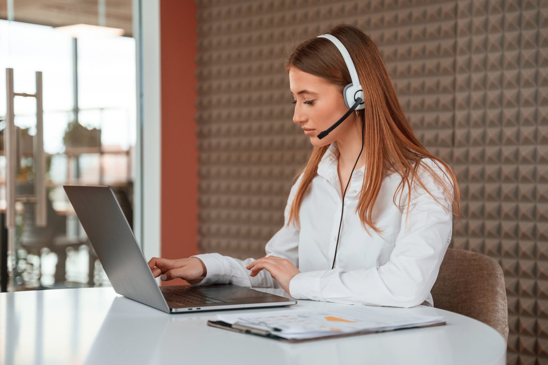 Customer support agent taking enquiries about Kitchen Worktop Sanding services while seated in an office with light oak hardwood plank flooring.