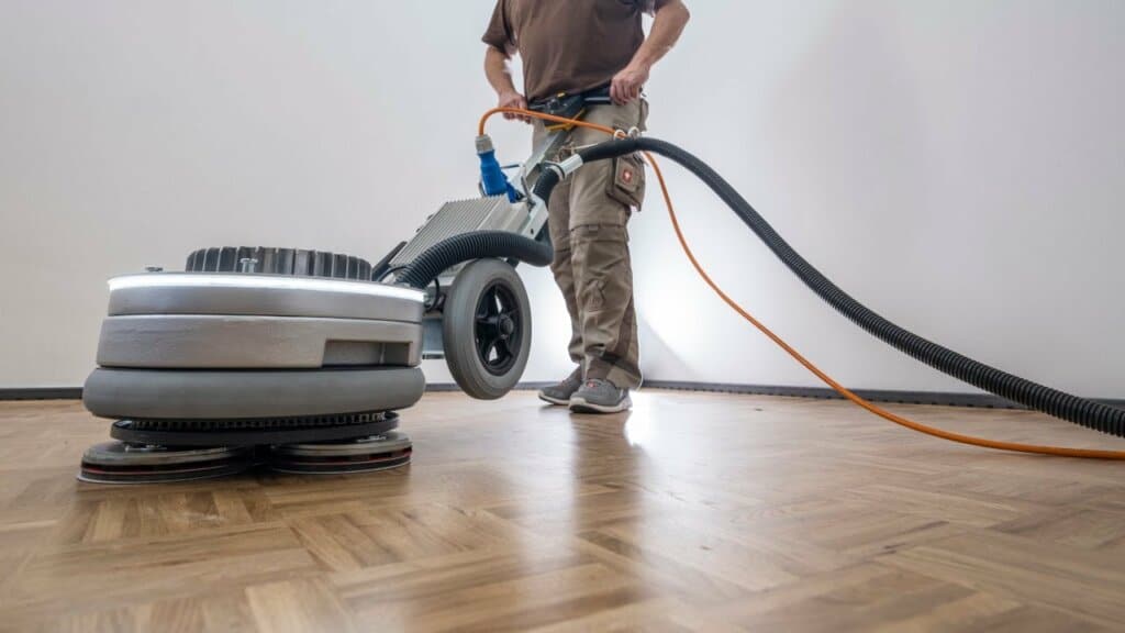 A man from Mr Sander® is sanding a parquet floor in a living room in Cudham, UK, using the Pallmann Spider. This easy-to-operate, 42 kg machine features triple-disc technology, 360° illumination, switchable power reserve, and infinite speed adjustment (50-400 RPM) for efficient sanding performance.