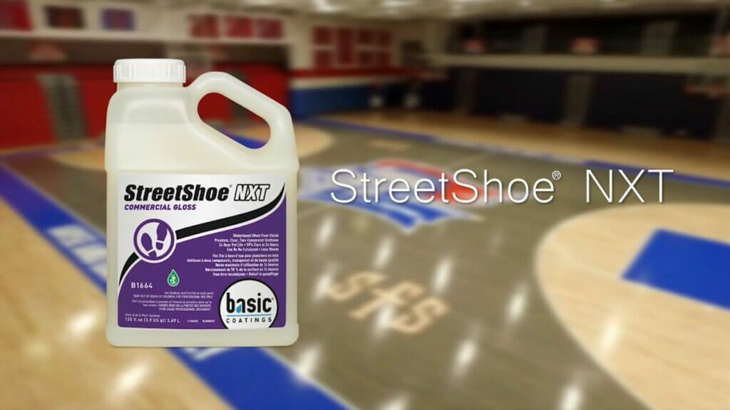 A jug of StreetShoe NXT commercial gloss wood floor finish on a blurred background of a gymnasium.