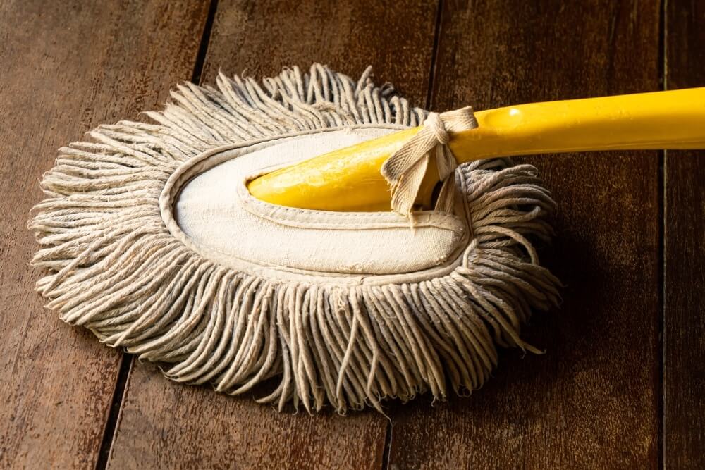 A yellow-handled mop with a soft cotton head used for cleaning a dark-stained, professionally refinished wooden floor.