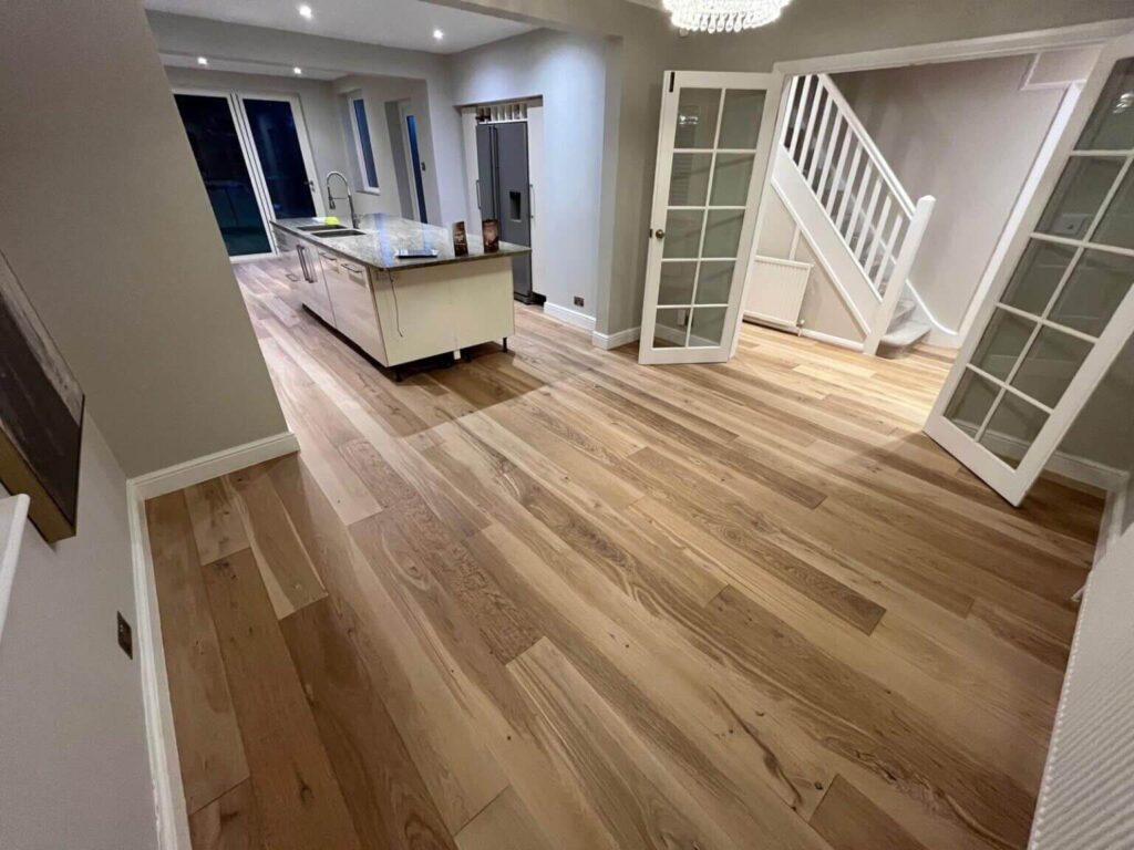 Freshly fitted wide-plank engineered oak flooring runs seamlessly through a modern open-plan London kitchen-diner and hallway, showcasing Mr Sander’s high-end installation craftsmanship.