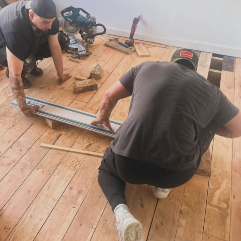 Two Mr Sander technicians levelling pine floorboards with a guide rail while repairing a timber floor