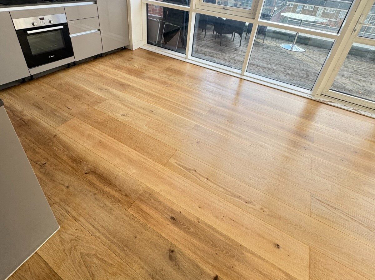 A wide-angle shot of a bright kitchen featuring an Oak Floor Revival with pale engineered oak planks, showcasing natural grain and a matte finish next to modern grey cabinetry.