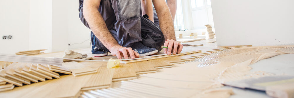 Mr Sander® fitter aligning slim oak parquet strips over fresh adhesive during an engineered hardwood floor installation.