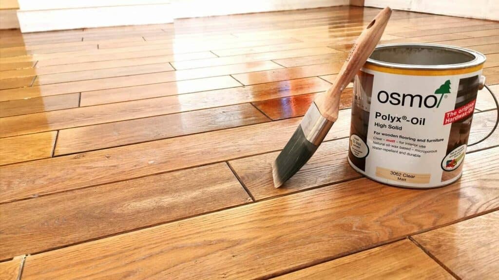 A can of Osmo Polyx-Oil next to a paintbrush on a freshly oiled wooden floor.