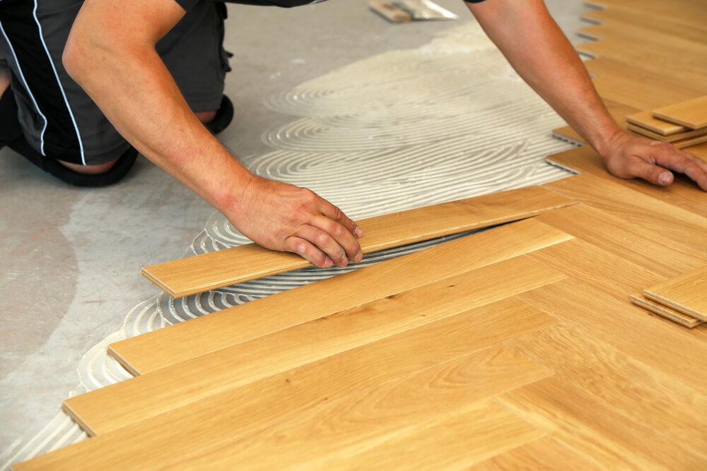 Parquet Borders being installed on an engineered oak herringbone parquet floor, installer aligning the border course over adhesive for a precise picture-frame edge.