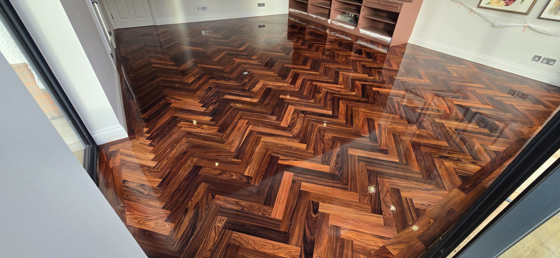Refinishing Parquet Flooring completed: high-gloss herringbone parquet with rich, dark tones and mirror reflection in a finished living room.