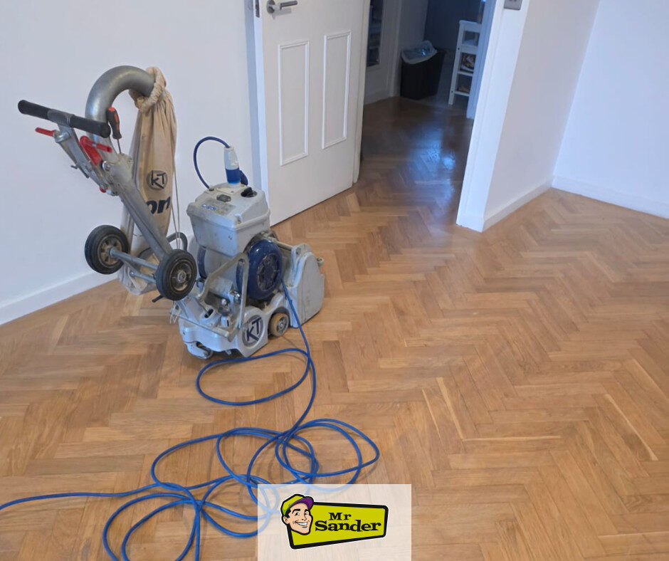 Parquet Floor Restoration — herringbone parquet being sanded with a professional belt sander and dust bag, floor leveled and ready for sealing.