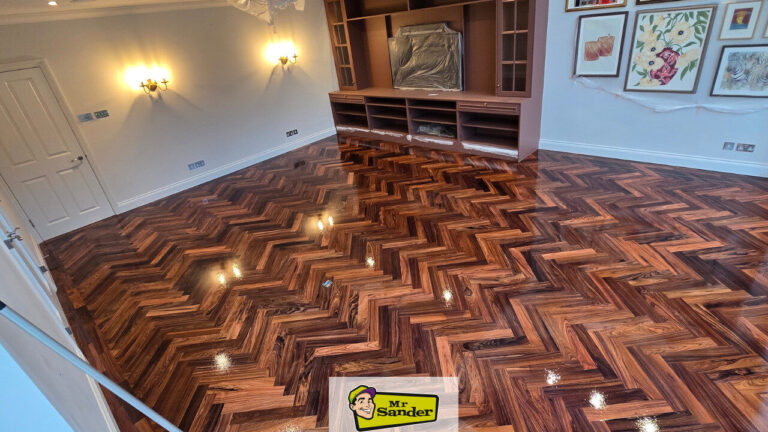 Parquet Floor Restoration — completed herringbone parquet in a living room, deep walnut stain and high-gloss lacquer giving a mirror-like finish with crisp, even pattern.