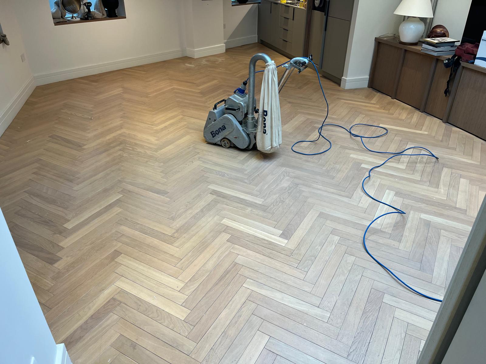 Professional Bona machine carrying out Parquet Floor Sanding on a light oak herringbone parquet wood floor in a modern living space.