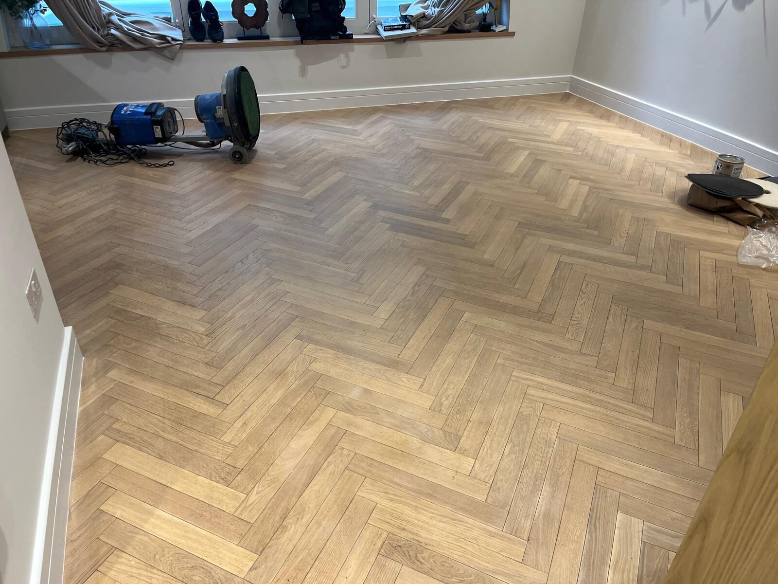 Parquet Floor Sanding on a light oak herringbone parquet wood floor, with sanding machines and finishing tools set out in a bright, modern room