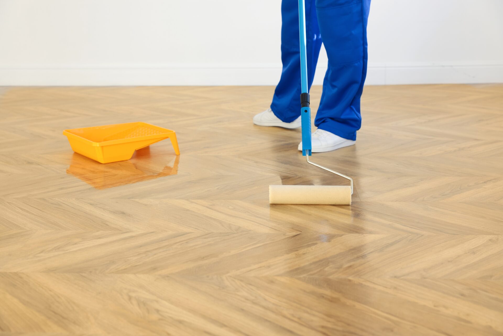 Technician applying lacquer with a roller to an oak herringbone parquet wood floor after professional Parquet Floor Sanding.
