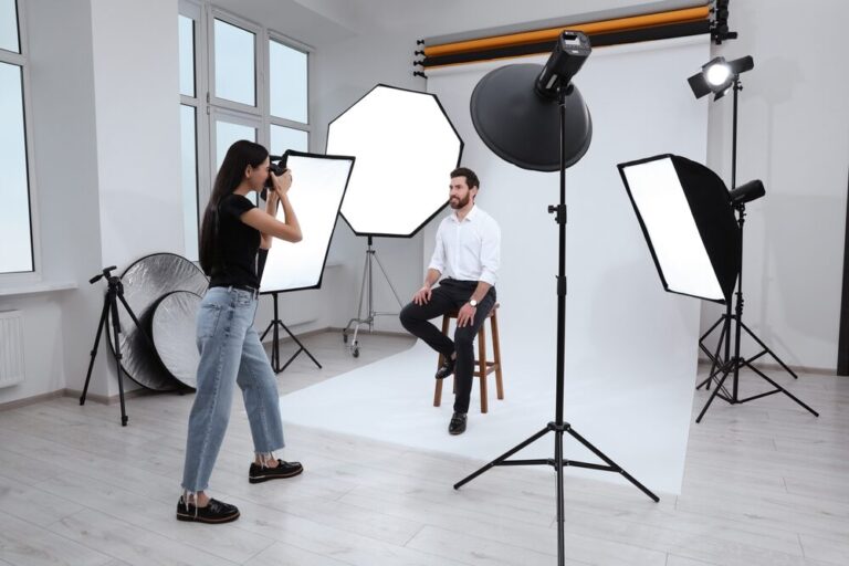 Floor Installation for Photographic Studios - Female photographer shooting a seated male model in a bright studio with octagonal and rectangular soft‑box lights, seamless white backdrop and a light‑grey engineered wood floor that minimises glare