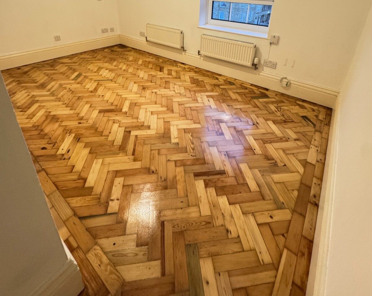 Restored pine herringbone parquet wood floor with Border Strips framing the edges of an empty, freshly decorated room.