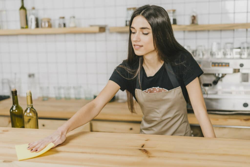 Woman cleaning a wooden kitchen counter with a yellow cloth.