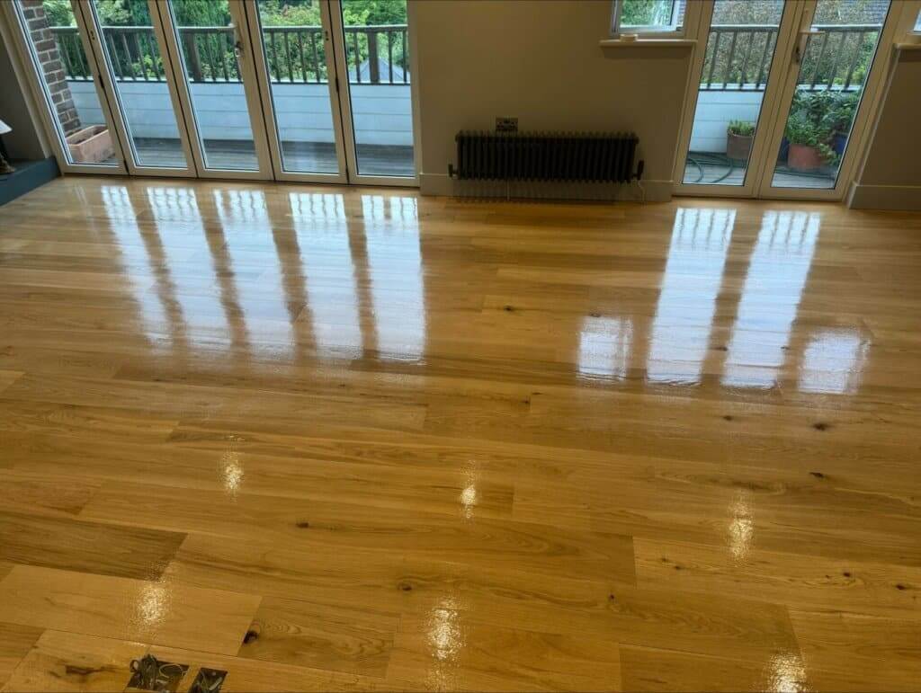Brightly polished wooden floor in a room with large windows overlooking a balcony.