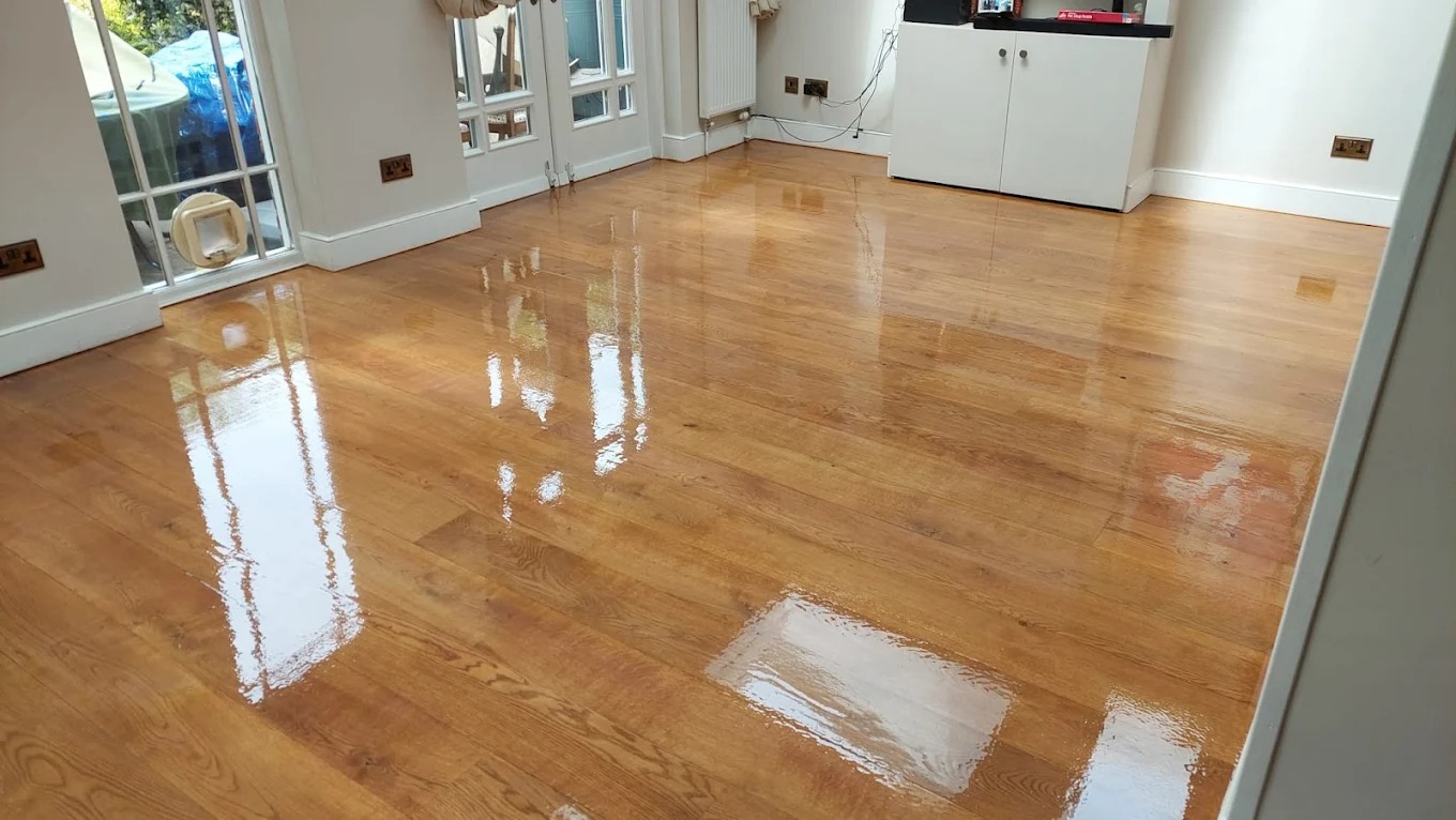 A freshly completed floor sanding project on oak hardwood flooring with a high-gloss finish reflecting light from a patio door.