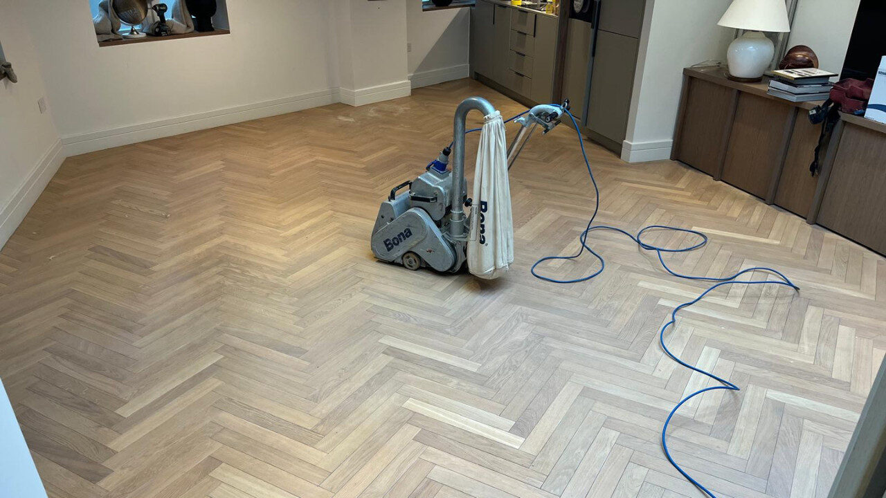 A heavy-duty Bona floor sander being used for professional sanding on an oak herringbone parquet floor to prepare it for finishing.