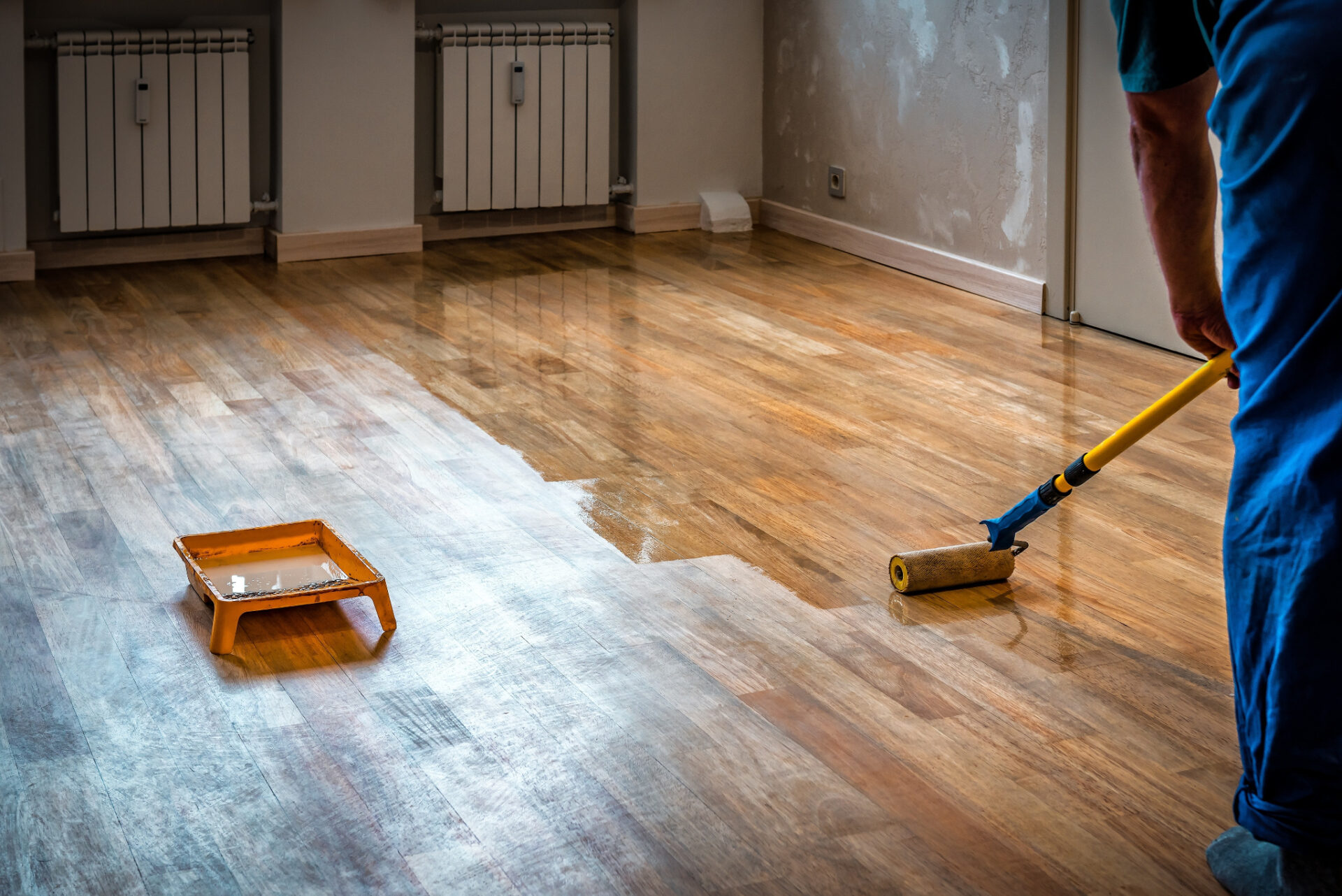 Professional applying a fresh coat to Recoat a Lacquered Floor on a lacquered hardwood plank wood floor, using a roller to restore a smooth, glossy finish. 