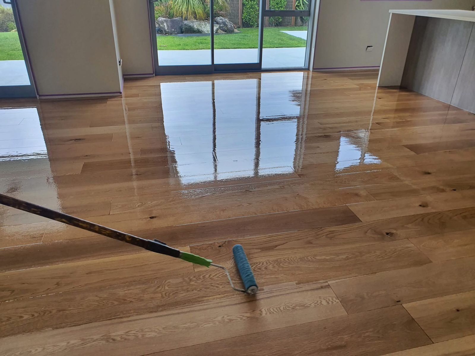 Roller applying a fresh coat to Recoat a Lacquered Floor on a lacquered solid oak hardwood plank floor, creating a smooth, high-gloss protective finish.
