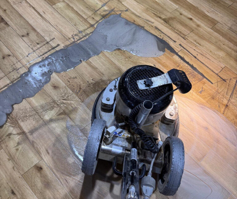 Close-up of a floor buffer wet-screening an oak floor with slurry to refinish floors without sanding before recoating.