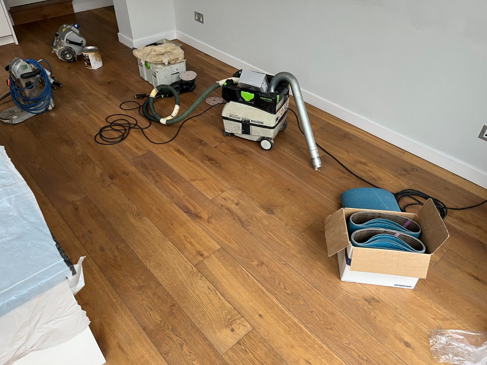 Refinish Hardwood Floors setup with sanding machines, dust extractor and abrasive belts on oak wide-plank engineered hardwood, ready for sanding and sealing.
