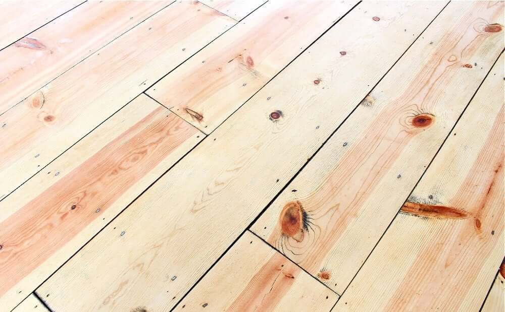 A close-up view of a newly refinished pine wood floor, showcasing the natural wood grain and knots.