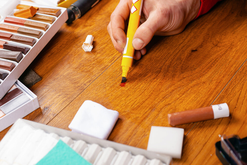 Repairing Scratches on Hardwood Floors with a touch-up marker—hand colour-matching oak boards beside wax sticks and pads