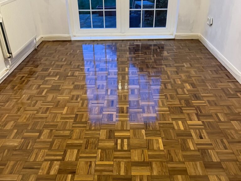 Close-up of a restored oak finger-block parquet floor near a patio door, showing the seamless fix for gaps and rich wood tones.