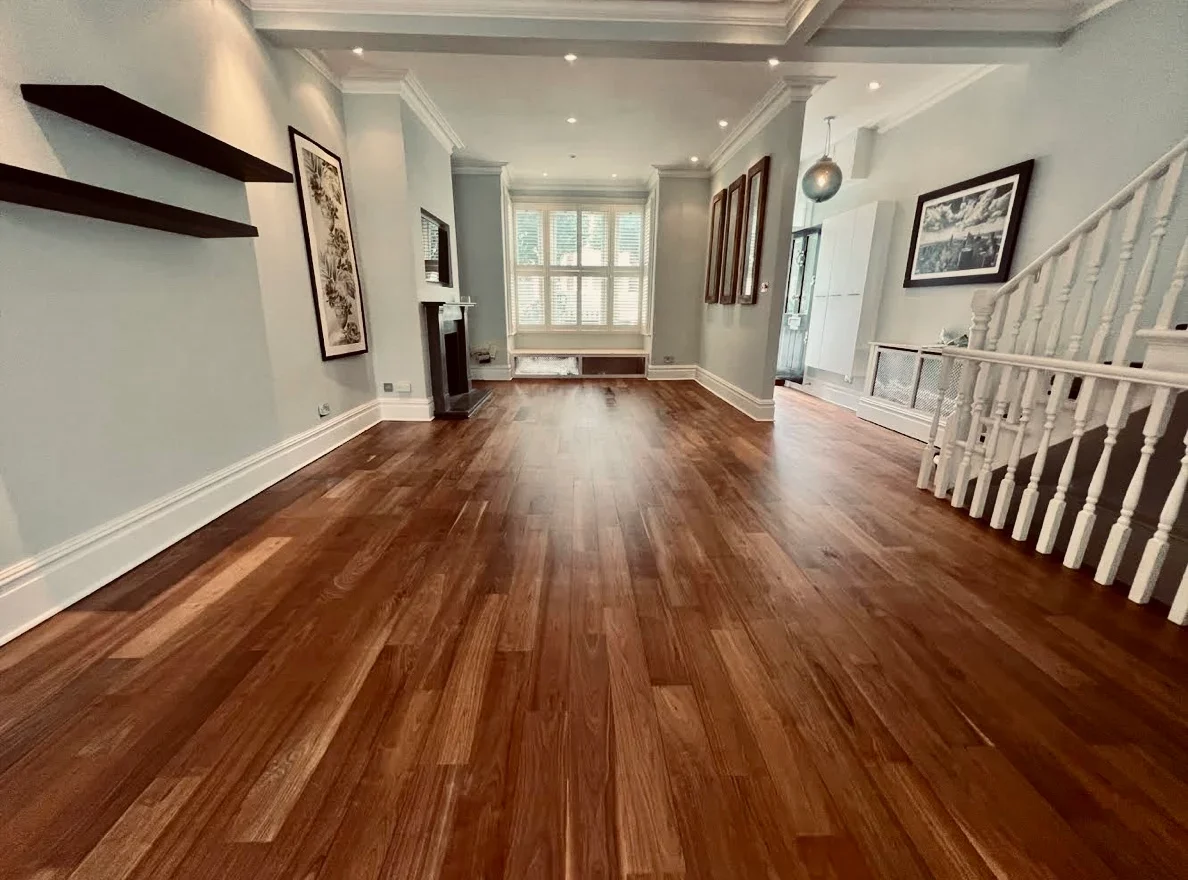 Restoring a Wood Floor: freshly refinished hardwood planks in a bright living room with bay window and staircase, showing a smooth satin finish after sanding and sealing.