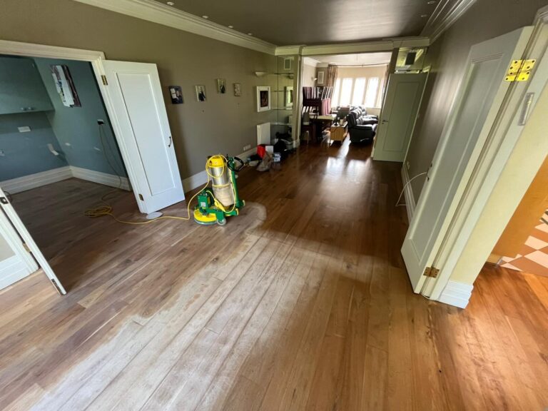 Restoring Floors in Listed Buildings: mid-sanding heritage oak hardwood plank floor in a period living room, showing freshly sanded pale timber beside finished boards and a professional floor sander.