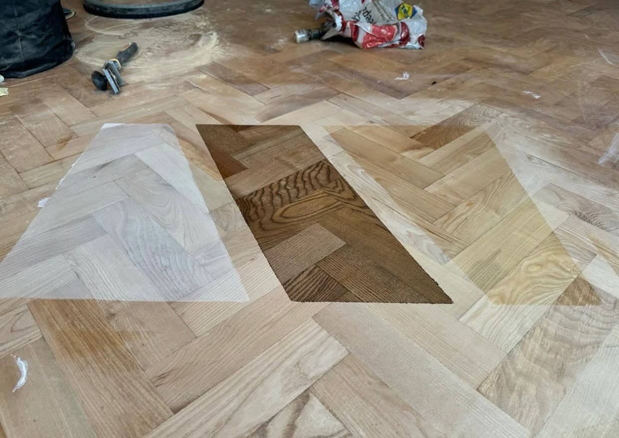 Restoring Parquet Flooring – stain/finish test patches on a freshly sanded herringbone oak parquet floor, comparing pale, natural and dark options before sealing.
