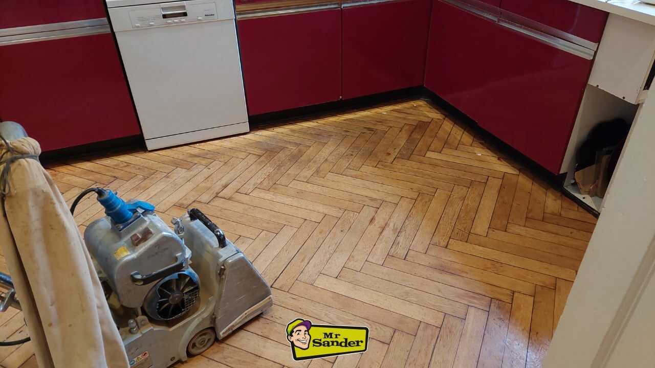 Restoring Parquet Flooring – drum sander on herringbone oak parquet in a kitchen, surface partly sanded and ready for edging and refinishing.