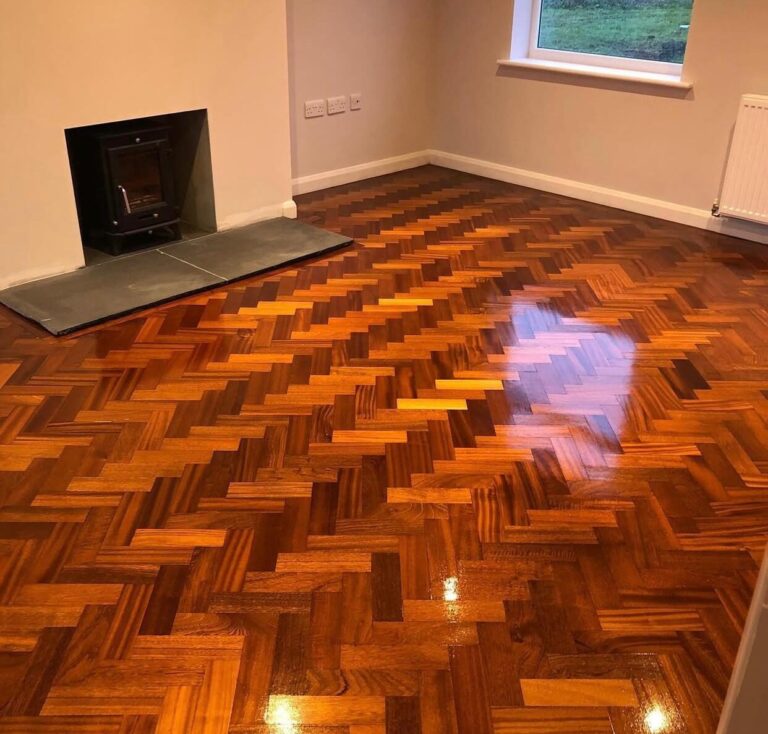 Restoring Parquet Flooring on a classic herringbone solid hardwood parquet—repaired, finely sanded, stained warm amber and sealed to a mirror-gloss finish beside a stove hearth.