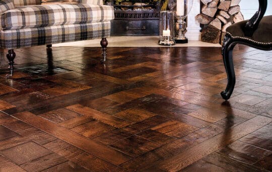 Detailed view of a herringbone patterned wooden floor with the legs of traditional furniture in a vintage setting.