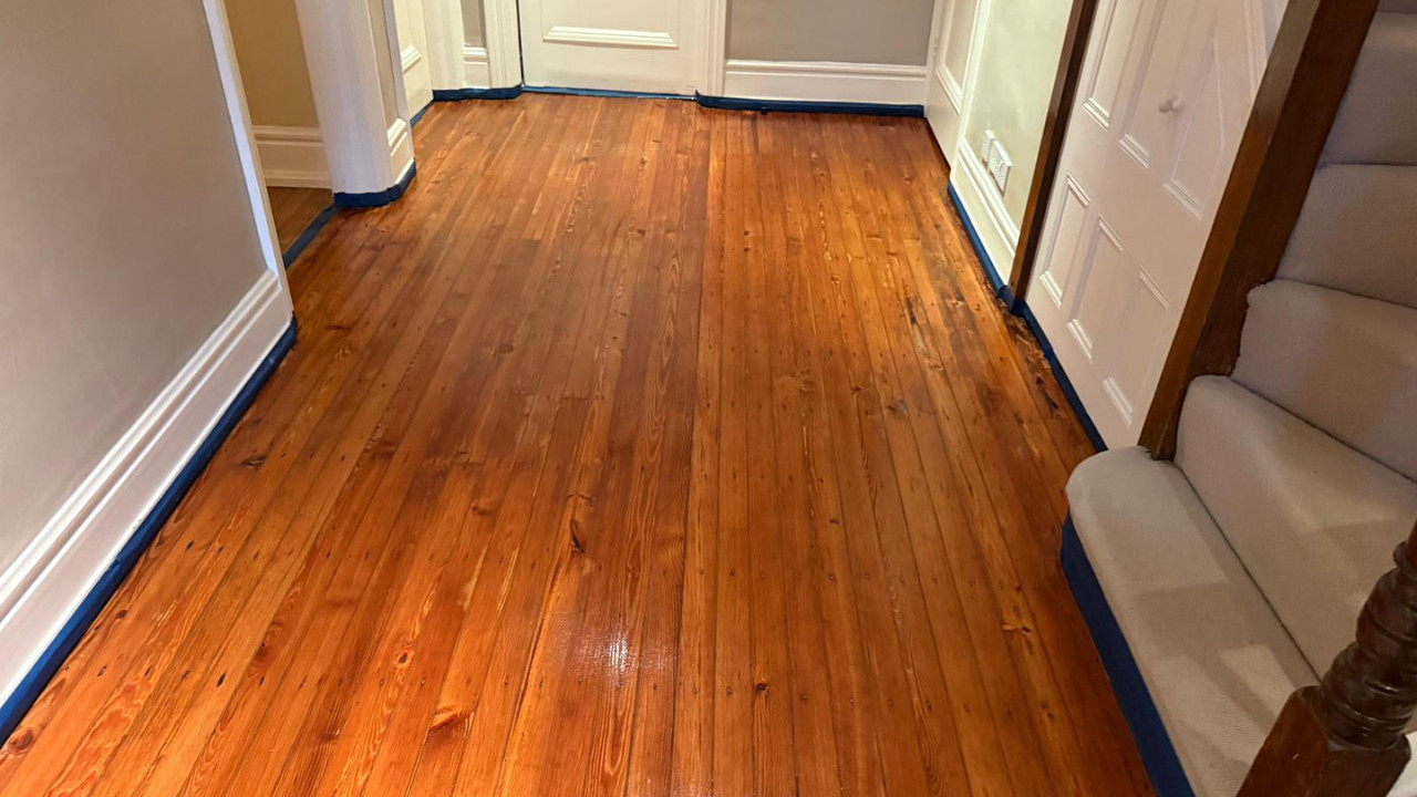 A freshly finished hallway featuring natural pine wood flooring with a warm amber stain, demonstrating the high-quality results achieved through professional sanding and refinishing.