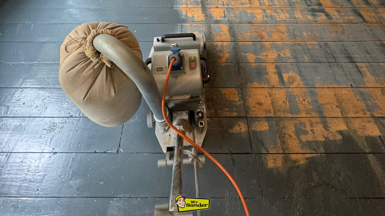Professional sanding machine stripping black paint from original pine floorboards (solid softwood) during the preparation stage before staining wood floors.