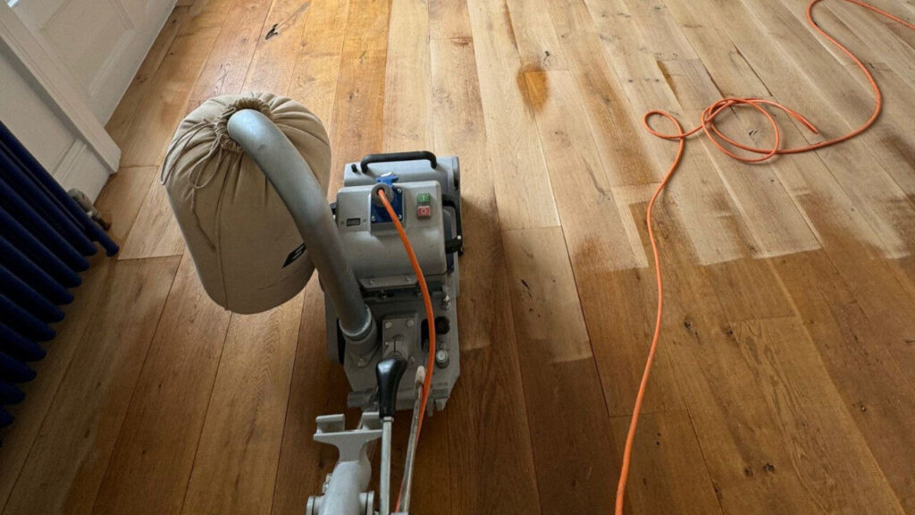 Drum sander in action on a solid oak floor—old finish removed and fresh timber revealed during sanding, staining and finishing wood floors.