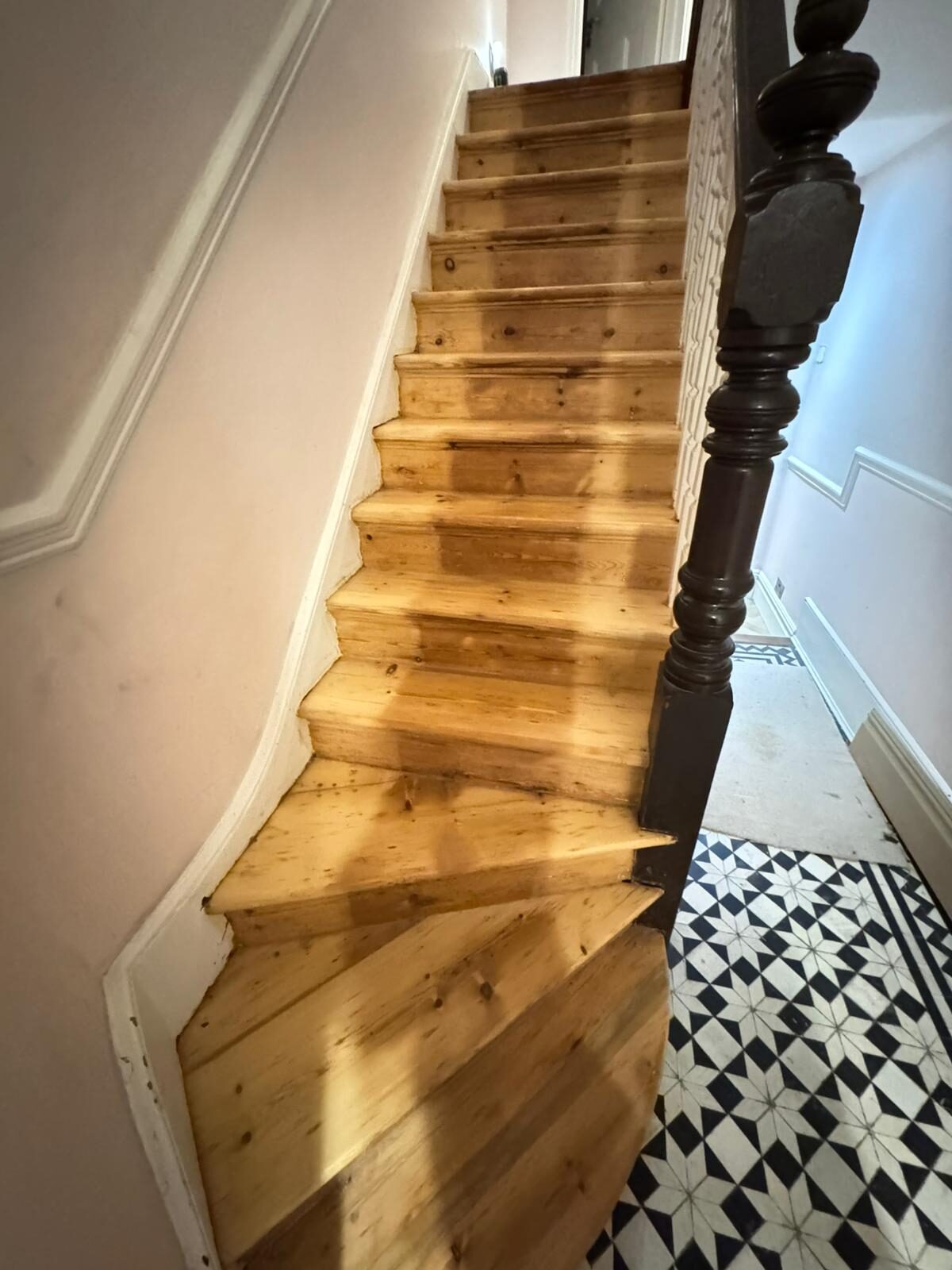 A full view of a classic wooden staircase featuring freshly sanded stair treads made of pine softwood, leading up from a decorative tiled floor.