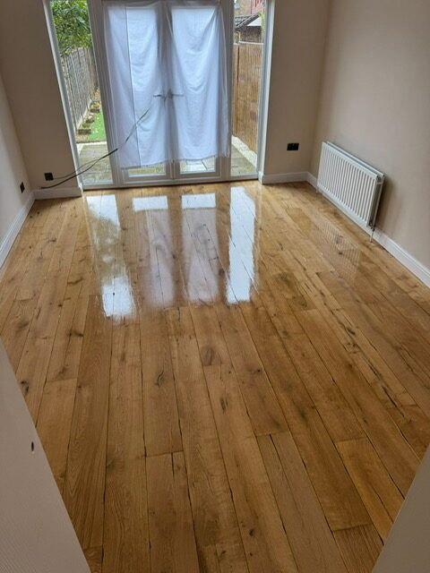 Sanding Wood Floors Successfully — freshly restored oak plank floor with a clear lacquer finish in a bright living room, showing a smooth, reflective surface after professional sanding.
