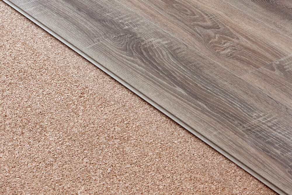 A laminate wood plank partially laid over cork underlayment